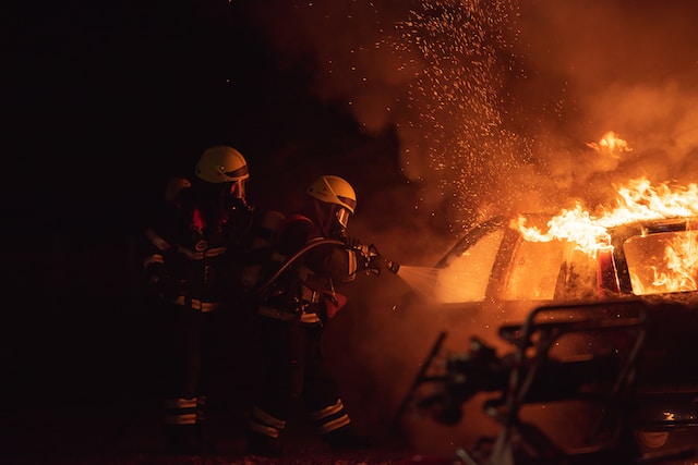 Two firefighters use a hose to put out a car fire